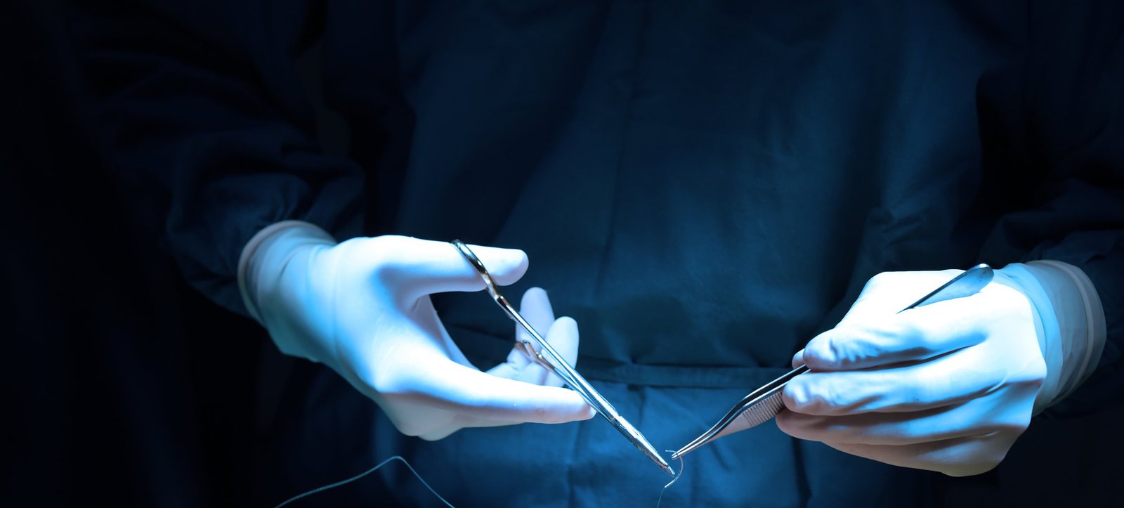Behandschuhte Hände halten ein chirurgisches Instrument im Operationssaal
